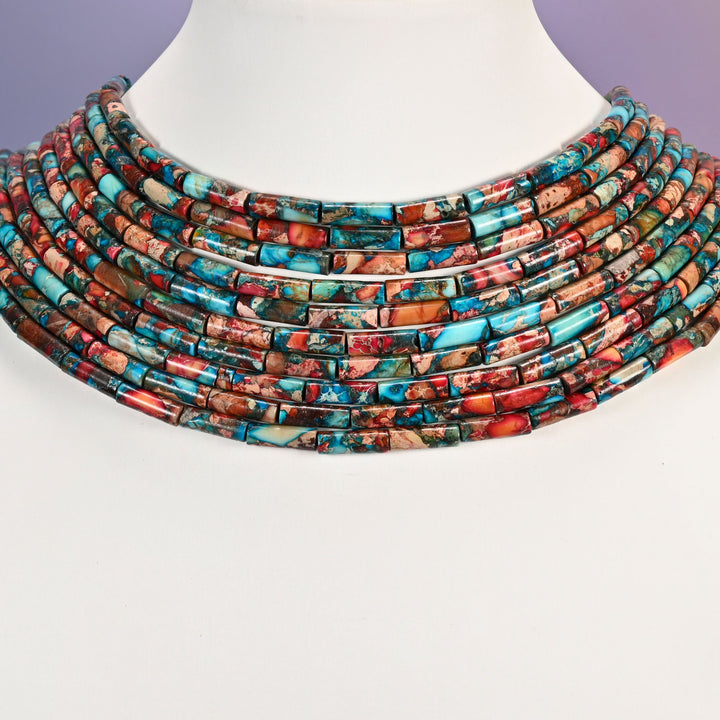 Multi-strand turquoise and coral jasper tube bead necklace laid flat on a mannequin neck form against a lavender background.