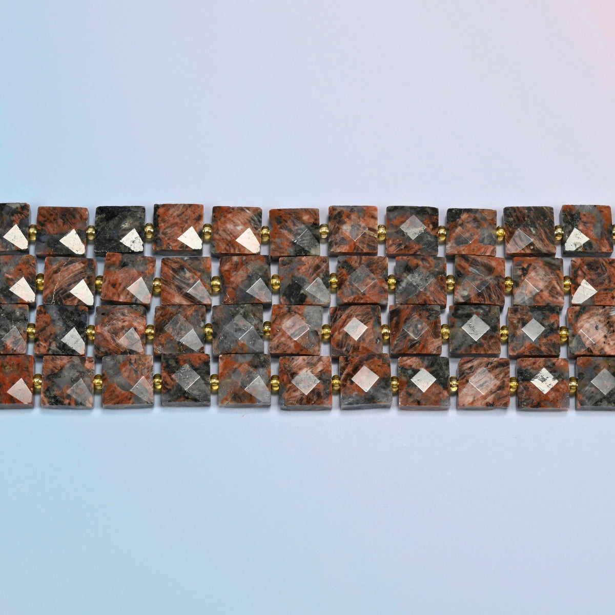 Several strands of natural red sesame jasper faceted flat square beads laid in straight rows