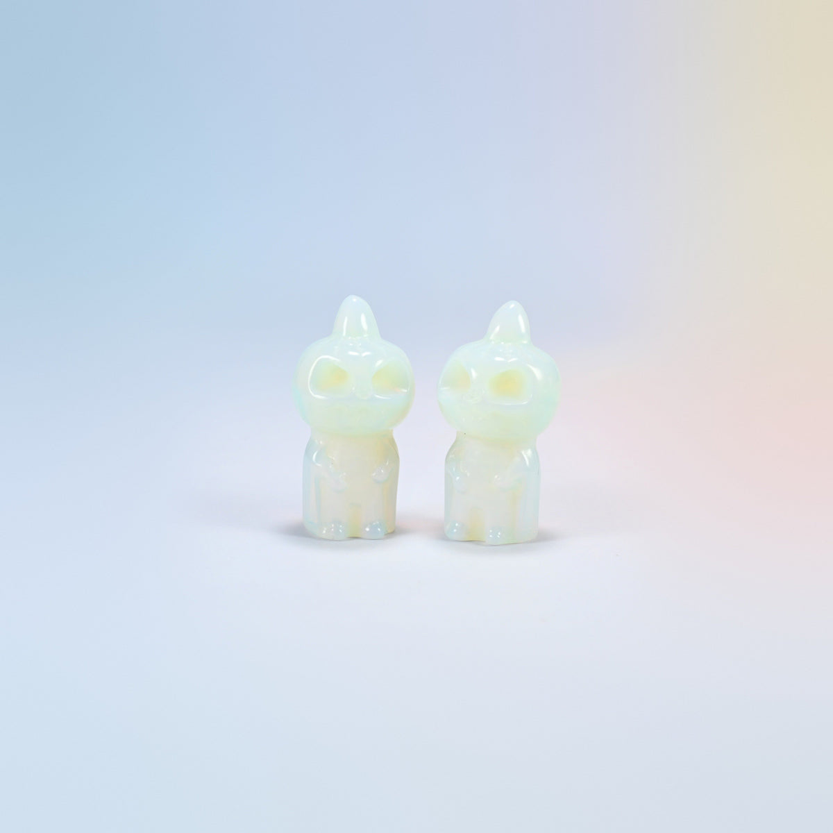 Two opalite pumpkin skull carvings with a milky glow and a soft blue sheen, man-made glass