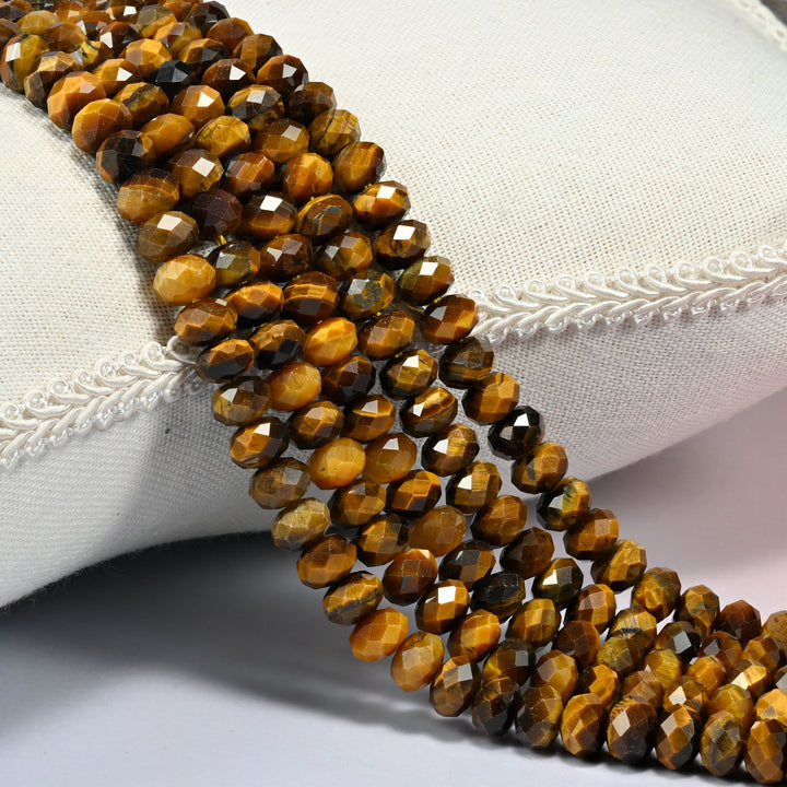 Tiger eye faceted rondelle beads in golden brown banded with dark brown, three strands draped over a cream linen cushion with braided trim