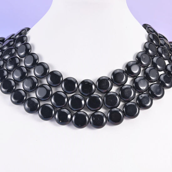 Black obsidian 15mm coins layered on a white display bust, four rows overlapping like a collar necklace