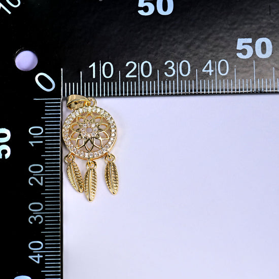 Gold Dream Catcher Zirconia Charm at the corner of a black millimeter ruler, feathers hanging down the scale for size reference.