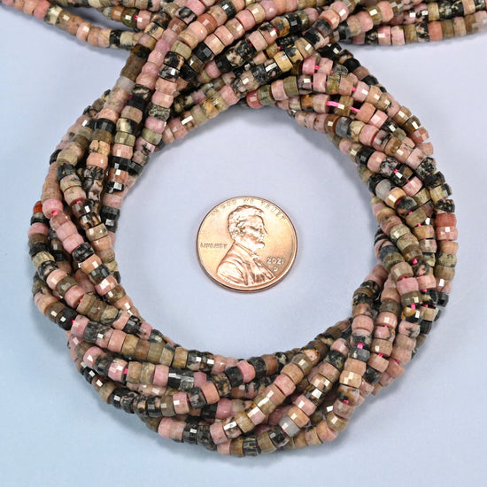 Rhodonite faceted heishi disc beads 2x4mm coiled in a loop around a US penny for scale, close-up of the faceted disc shape