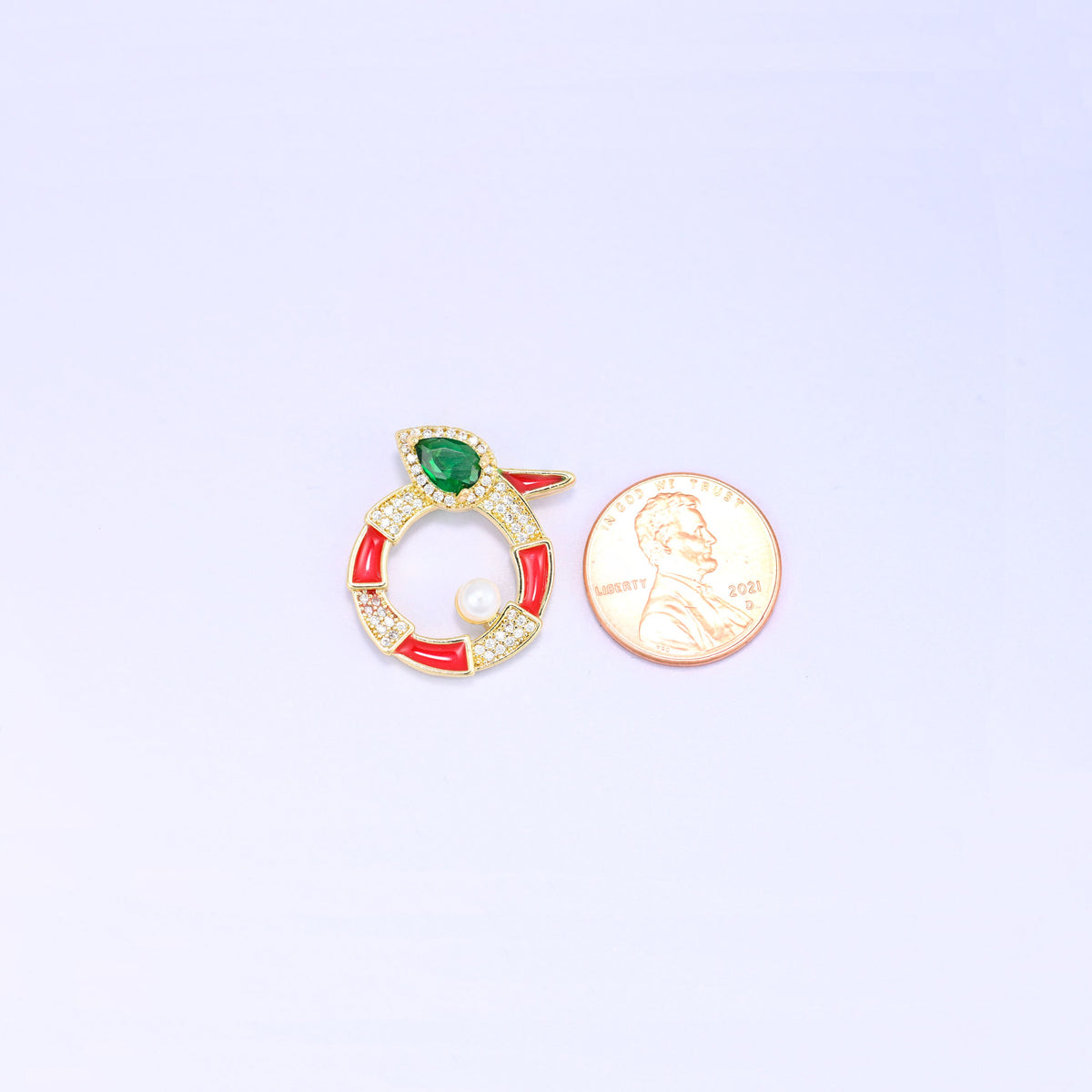 Scale shot of the round snake charm, the red enamel medallion photographed next to a US penny and slightly larger than the coin.