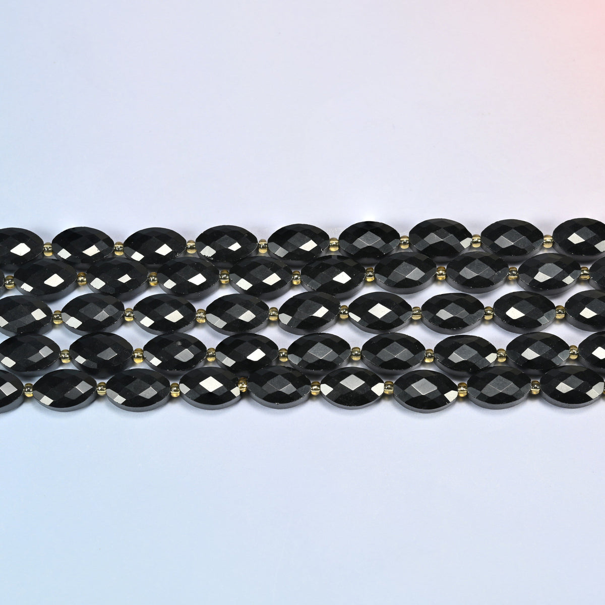Several strands of black onyx faceted flat oval beads laid in straight rows with gold seed bead spacers