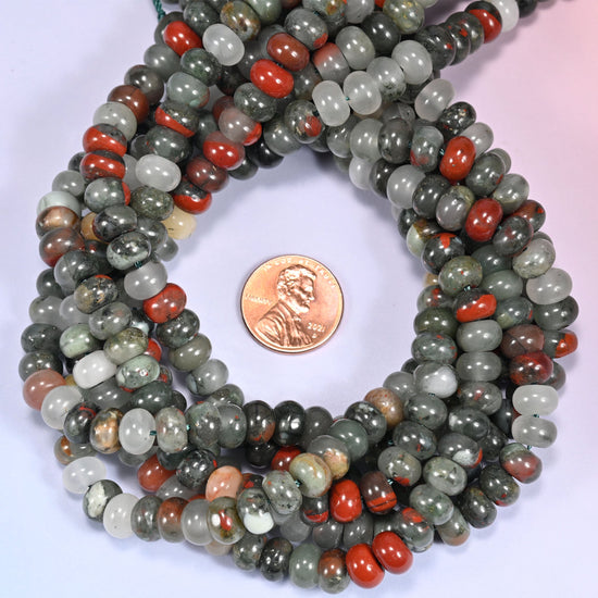 Multiple strands of African Bloodstone beads gathered together on a lavender surface, loose ends visible.