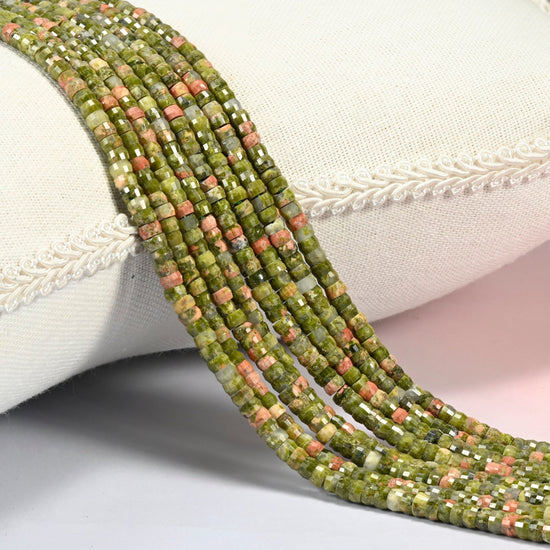 Unakite faceted heishi disc beads 2x4mm, several strands draped over a white cushion