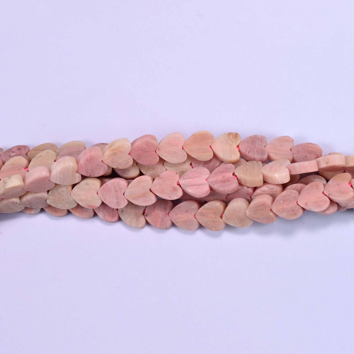 Matte pink rhodonite flat heart beads in dusty rose and antique pink drifting into oatmeal and pale beige.