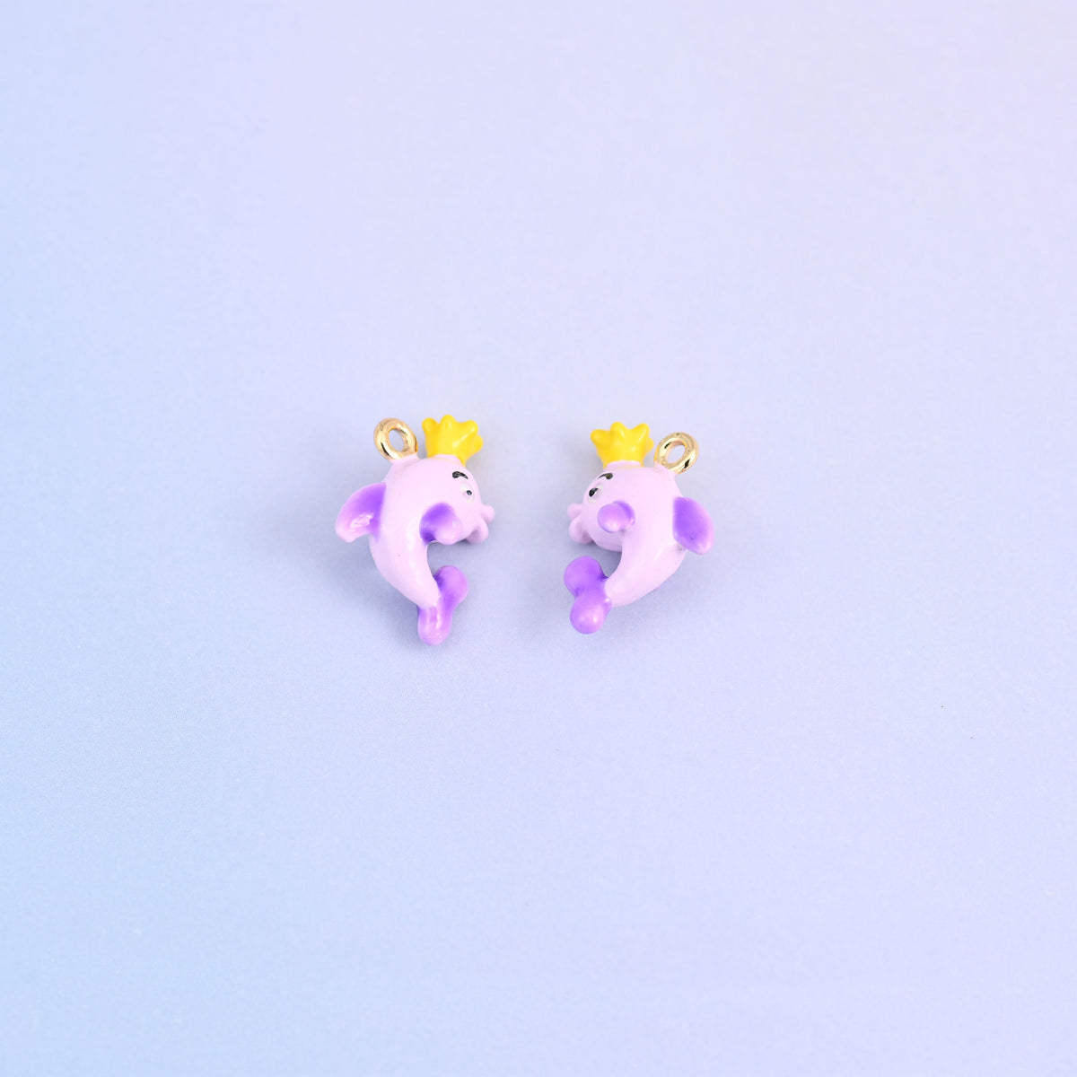 Two light purple dolphin charms with crowns, front and back, each wearing a yellow crown.