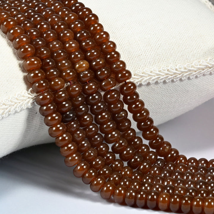 Chestnut Brown dyed jade gemstone rondelle beads draped over a cushion in soft rows, a rich warm chestnut brown under a glossy polish