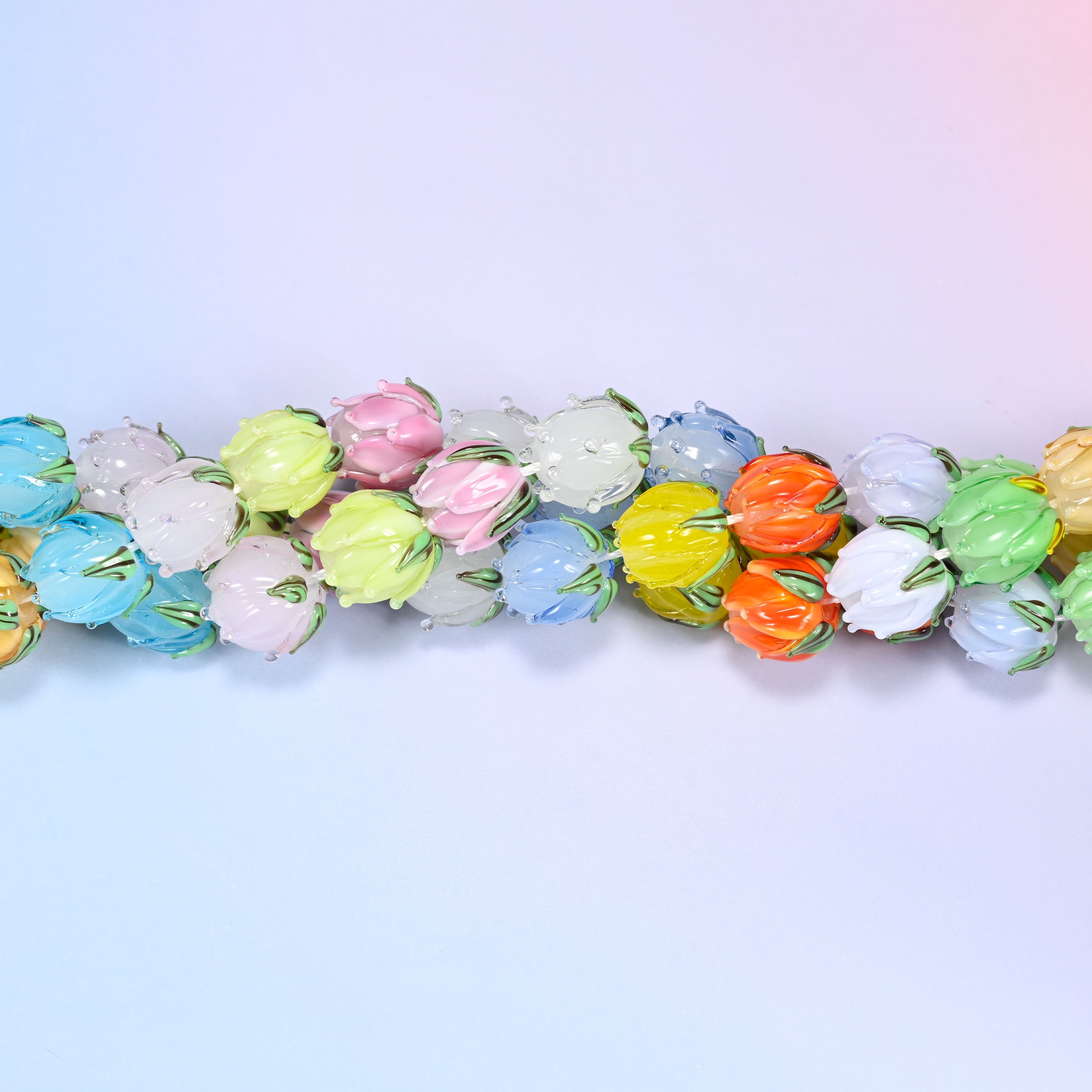 Wide circular coil of multicolor tulip bud lampwork glass bead strands forming a full wreath shape on a lavender and pink gradient background.
