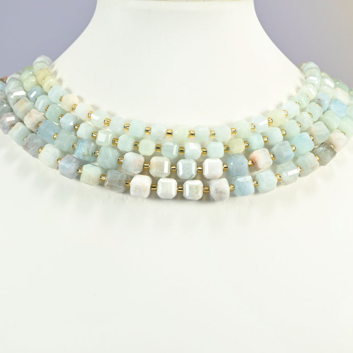 Aquamarine faceted cube beads on a white neck display, four strands layered around the base.