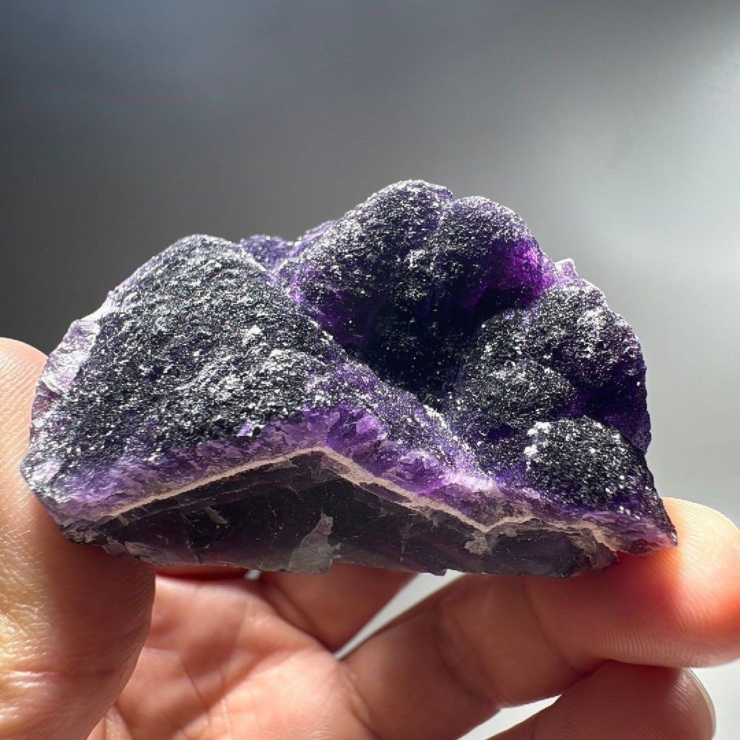 Dark purple fluorite specimen held in hand, druzy quartz crust over a glassy cleaved base.