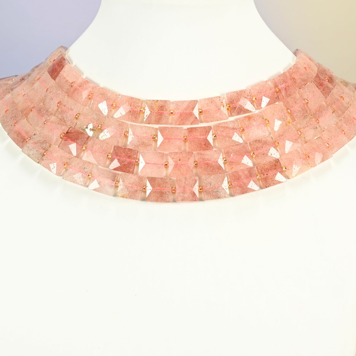 Natural strawberry quartz faceted flat square strands arranged as a layered collar on a white display bust, soft pink beads across the neck