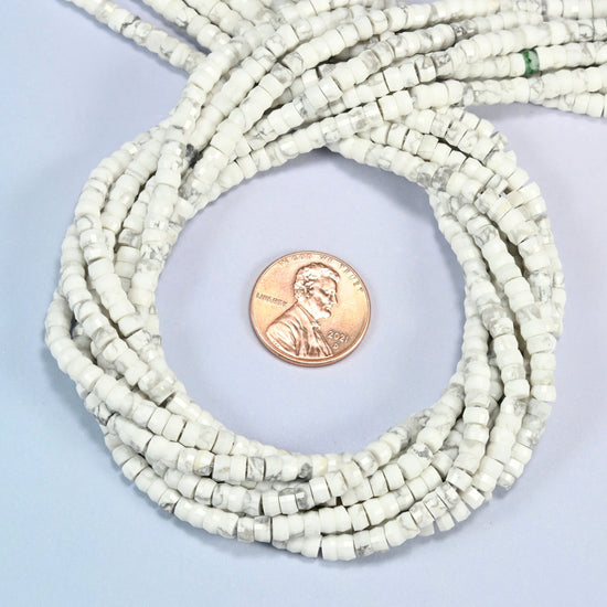 White howlite faceted heishi disc beads 2x4mm coiled in a loop around a US penny for scale, close-up of the faceted disc shape