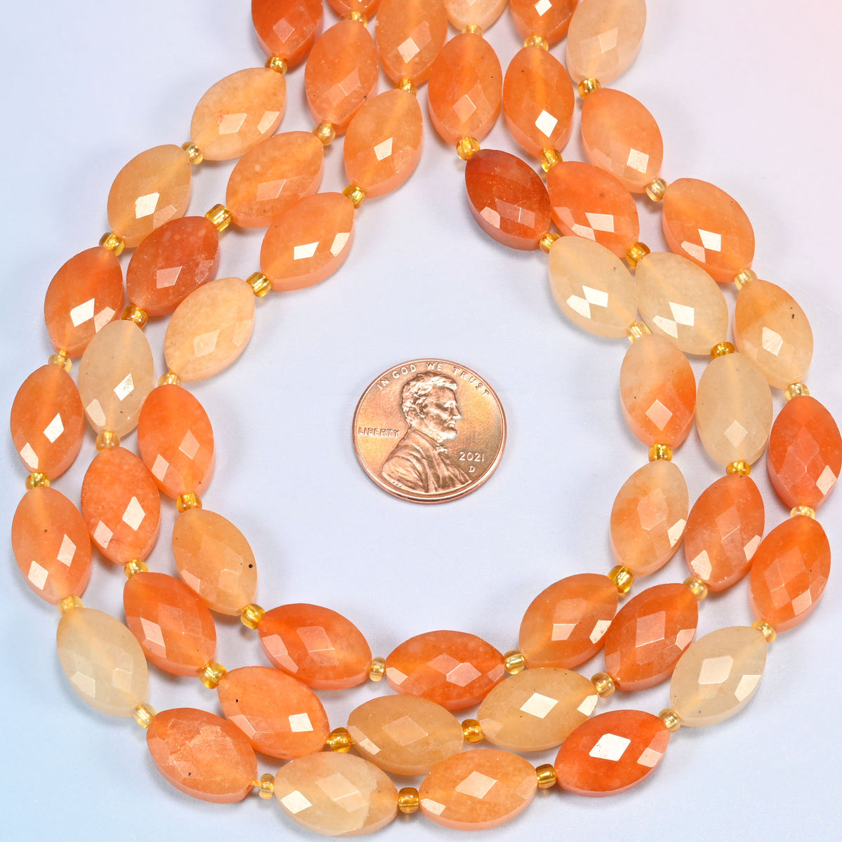 Red aventurine faceted flat oval strands formed into a teardrop loop around a US penny for scale