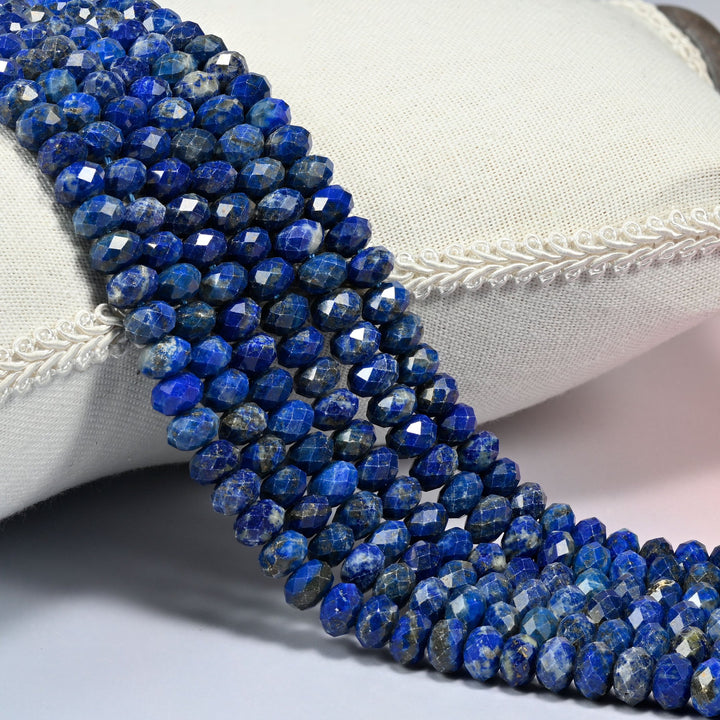 Lapis lazuli faceted rondelle beads 5x8mm in deep royal blue with white and gold flecks, several strands draped over a white cushion