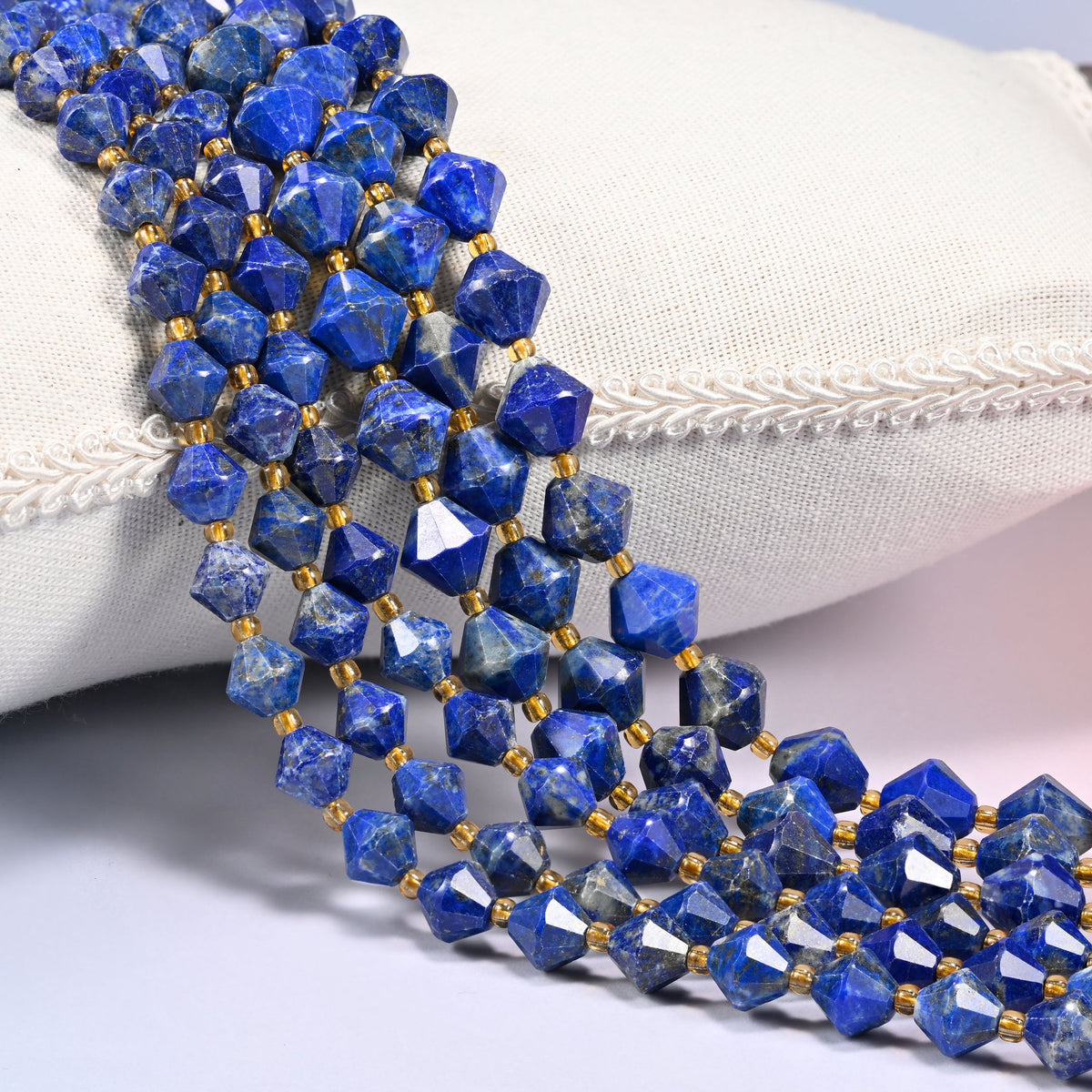 Lapis lazuli bicone beads laid out on the diagonal in several rows, deep blue with natural lighter mottling, a gold-tone spacer between every bead.