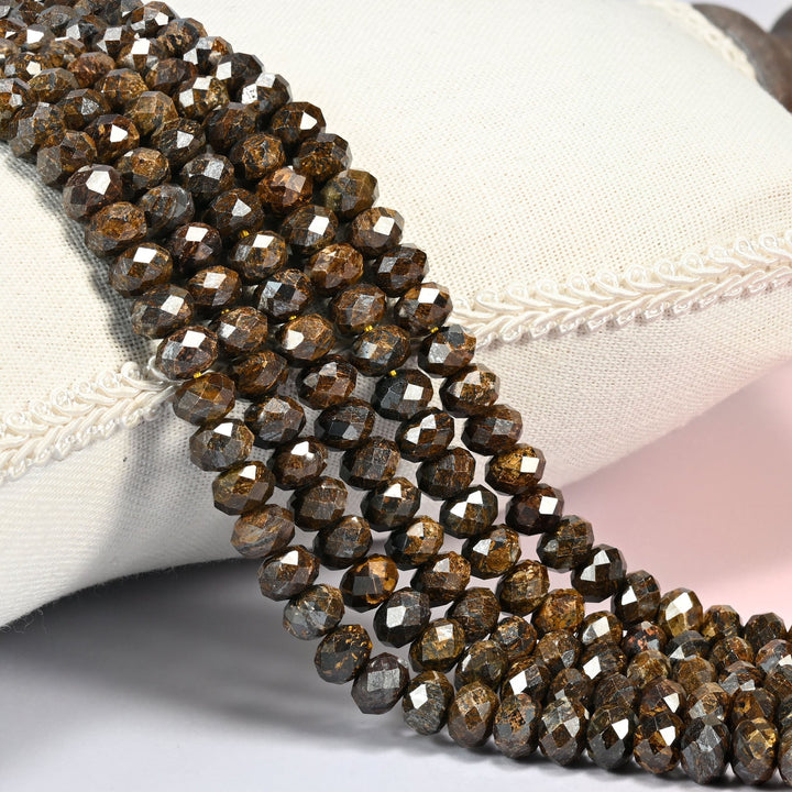 Bronzite faceted rondelle beads 5x8mm in dark chocolate brown flecked with golden bronze, several strands draped over a white cushion