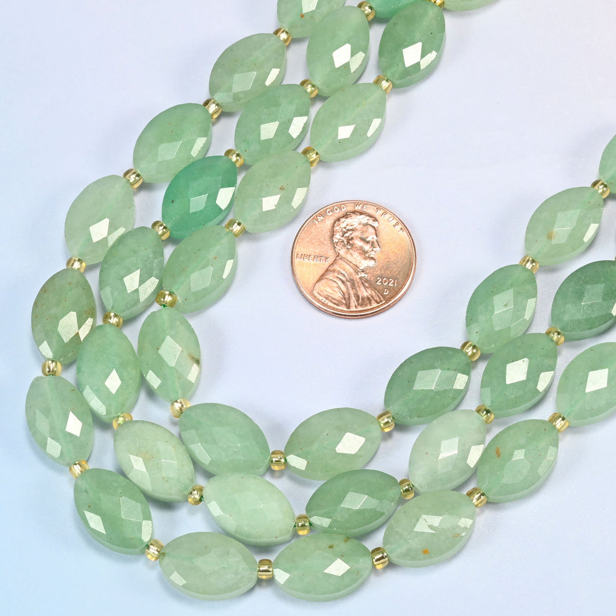 Close view of green aventurine faceted flat oval strands curving beside a US penny for scale