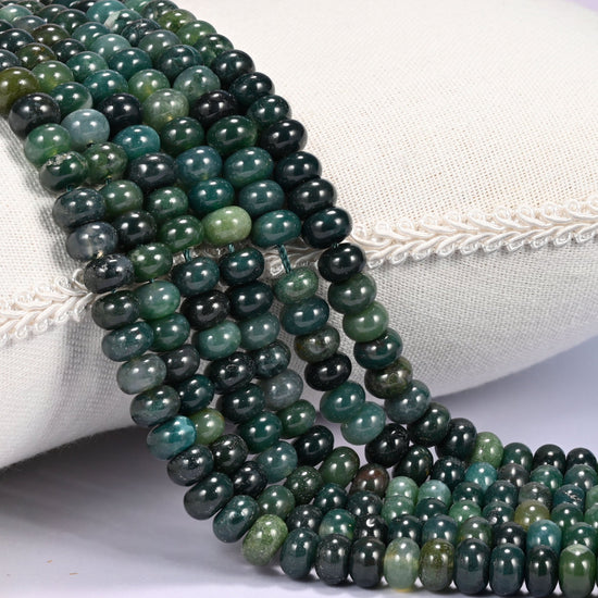 Close-up of multiple strands of polished Moss Agate rondelle beads in translucent green tones, draped over a cream fabric jewelry display bust.