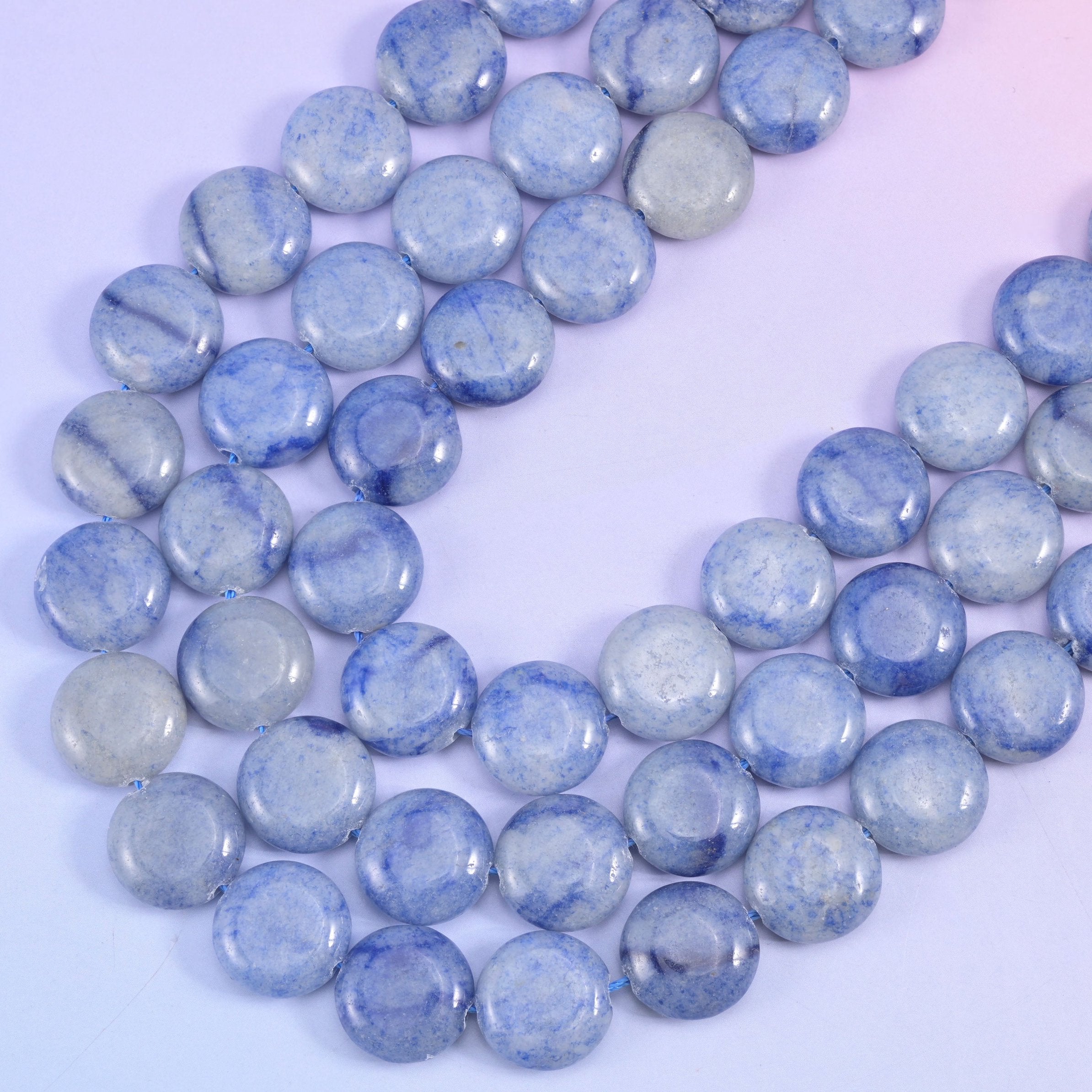 Two blue aventurine strands angling across lilac, showing the flat coin profile and softly rounded edges