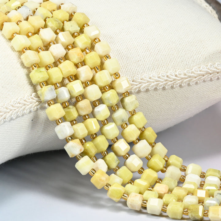 Butter jade faceted cube beads over a white cushion, soft yellow cubes with gold seed spacers.