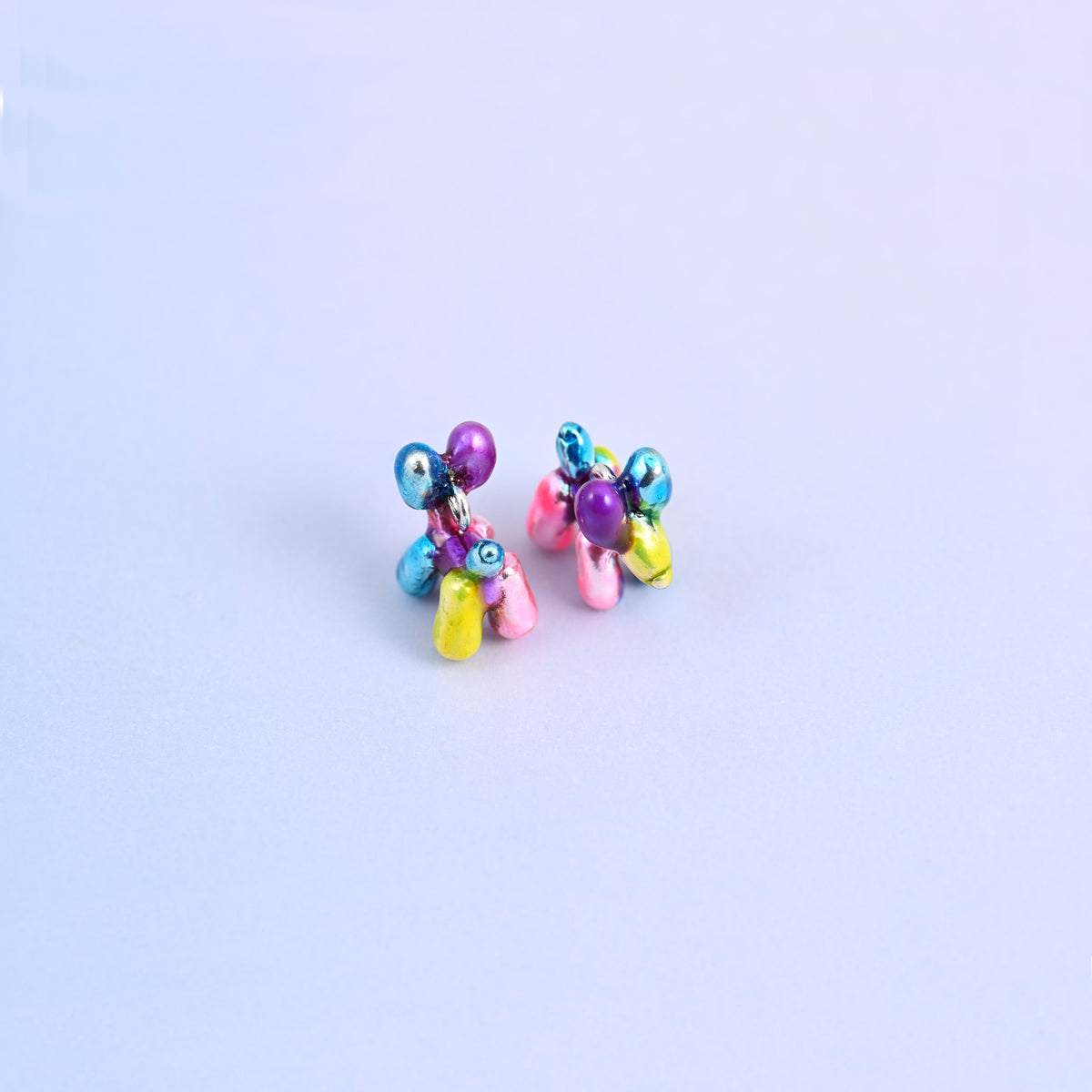 Balloon dog charms in close up, glossy metallic enamel over brass with a plated ring at the neck.