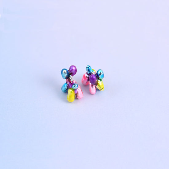 Balloon dog charms in close up, glossy metallic enamel over brass with a plated ring at the neck.