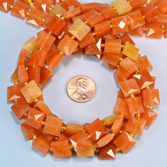 Natural red aventurine faceted flat square beads 10x10mm coiled in a loop around a US penny for scale, close-up of the faceted flat square shape