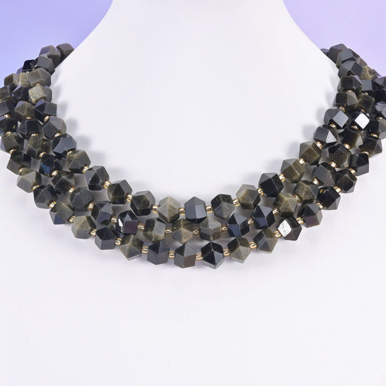Faceted 8 sides diamond rhombus beads in gold obsidian on a white neck display, three strands of near black stone.