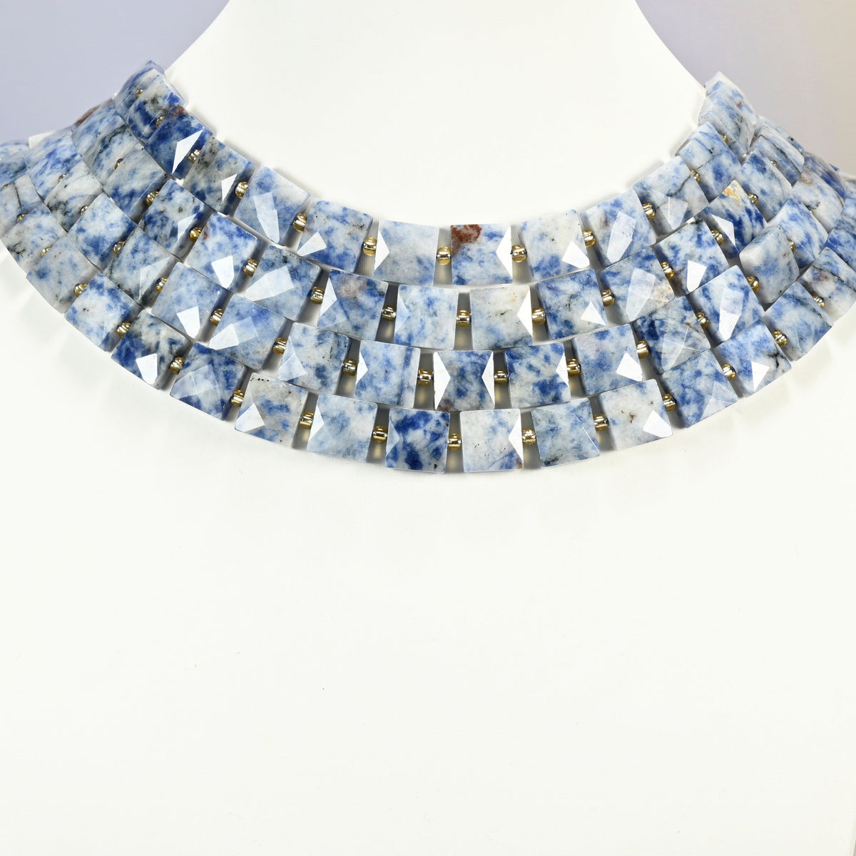 Natural blue spot jasper faceted flat square strands arranged as a layered collar on a white display bust, blue and white beads across the neck