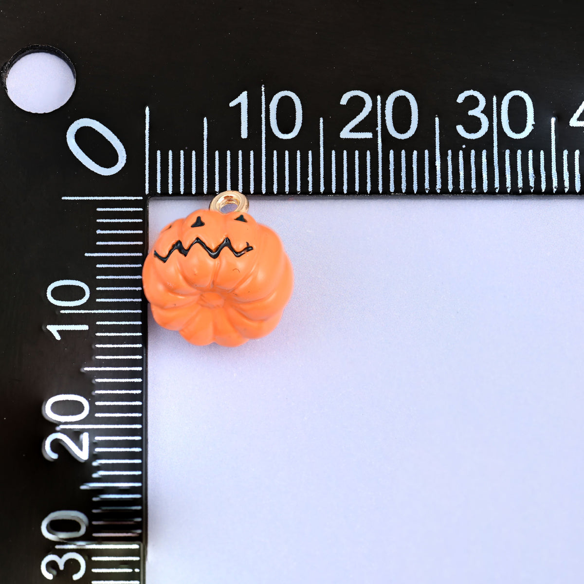 Enamel pumpkin charms shown with the jack o lantern face, 12.57 x 13.21mm including the gold-tone ring.