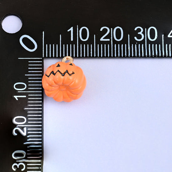 Enamel pumpkin charms shown with the jack o lantern face, 12.57 x 13.21mm including the gold-tone ring.