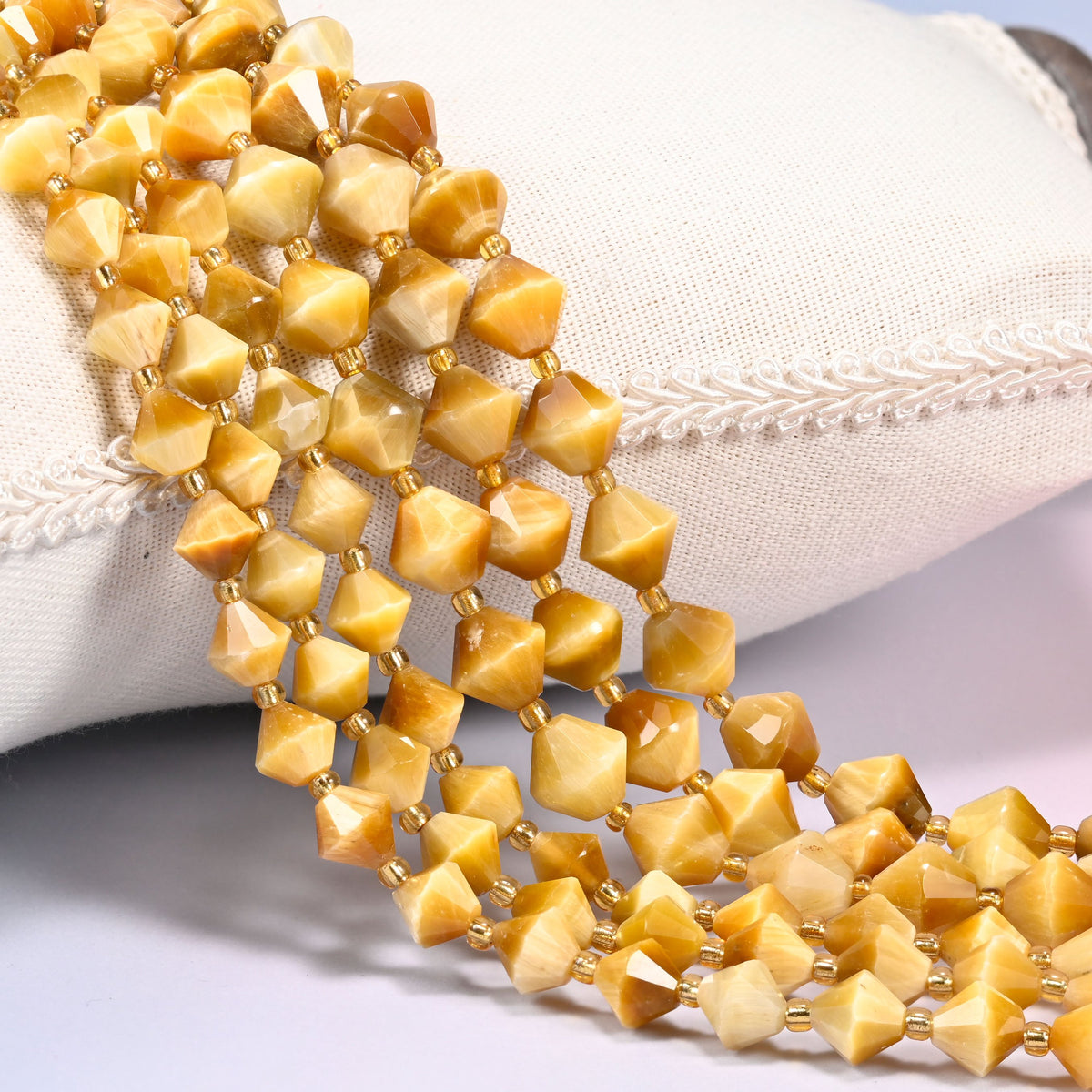 Gold tiger eye bicone beads laid out on the diagonal in several rows, golden honey brown with a silky chatoyant band, a gold-tone spacer between every bead.