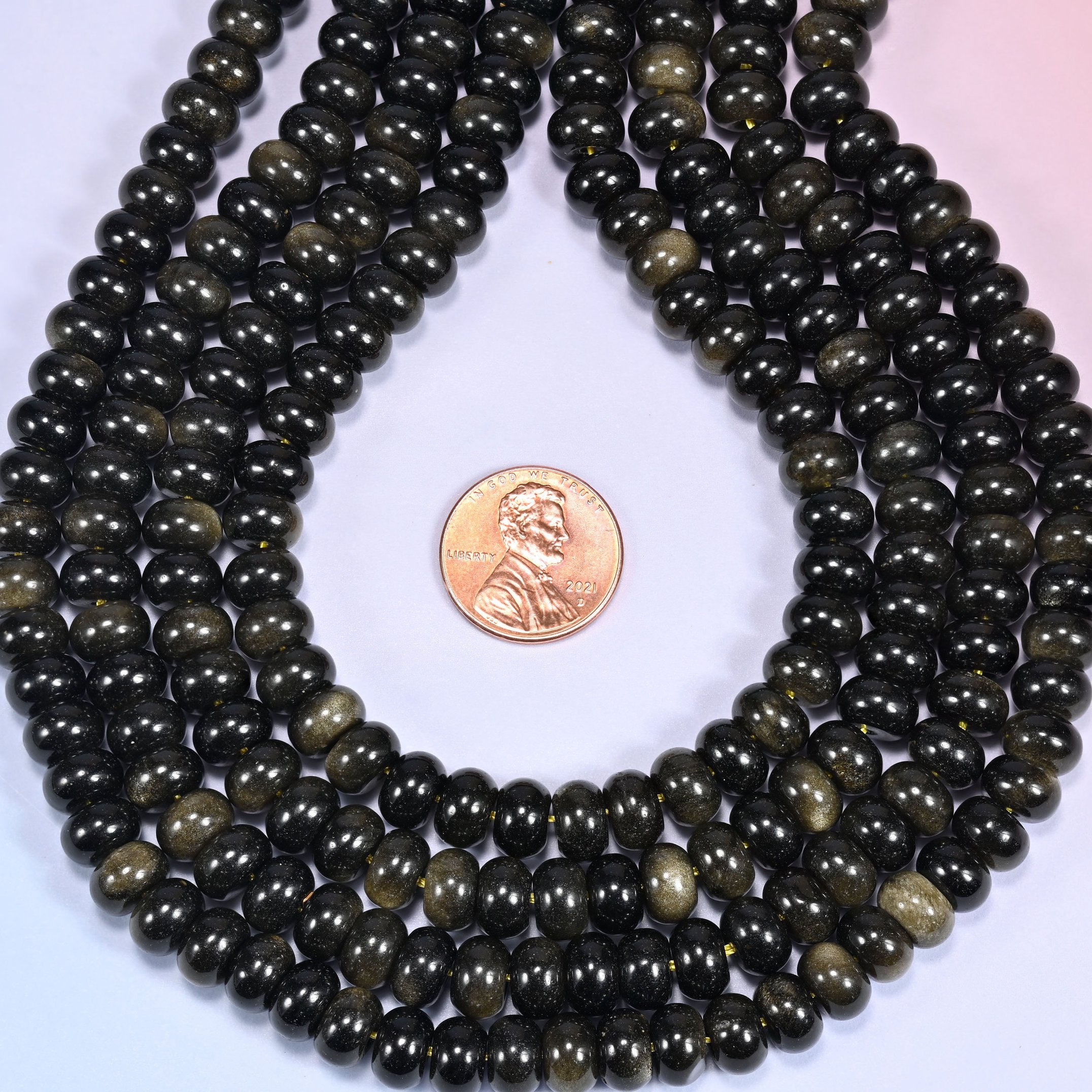 Bundled coil of Gold Obsidian rondelle beads on a lavender background with a penny placed at the center for scale.