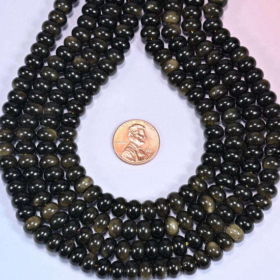 Bundled coil of Gold Obsidian rondelle beads on a lavender background with a penny placed at the center for scale.