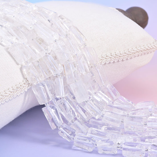 Ice-clear Clear Quartz faceted tube beads spilling from a cream cushion, light passing right through the 14x9mm rectangles