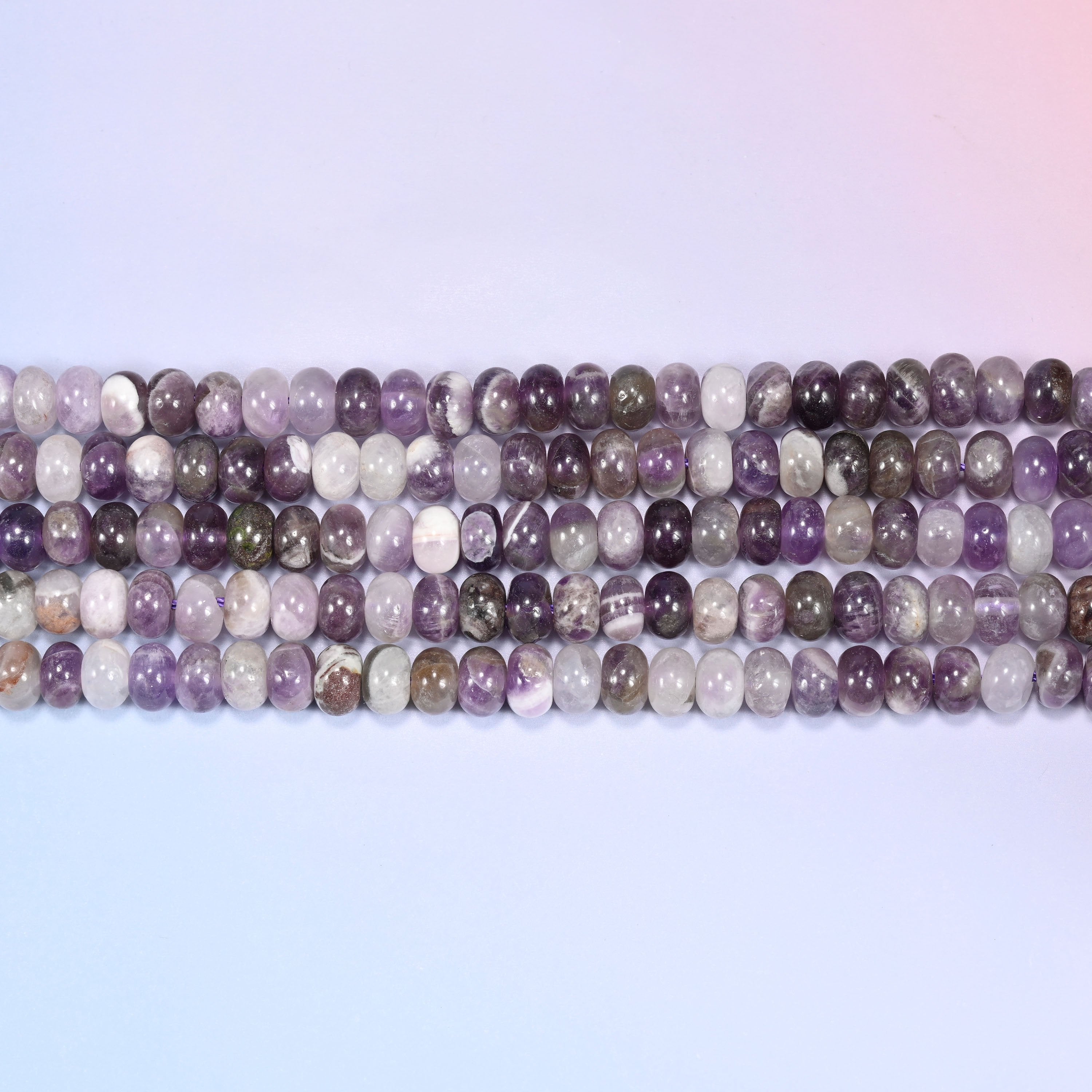 Overhead view of several rows of Amethyst rondelle beads showing the purple and gray-brown coloring on a light lavender surface.