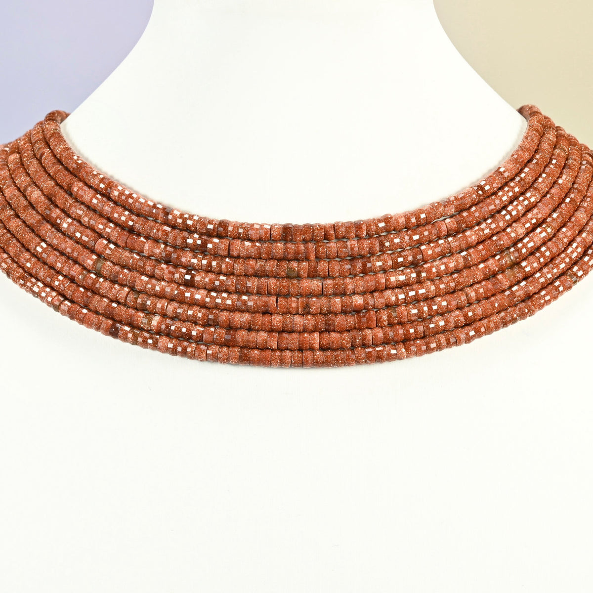 Gold sandstone faceted heishi disc strands arranged as a layered collar on a white display bust, copper brown beads across the neck