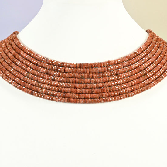 Gold sandstone faceted heishi disc strands arranged as a layered collar on a white display bust, copper brown beads across the neck