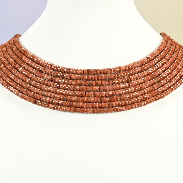 Gold sandstone faceted heishi disc strands arranged as a layered collar on a white display bust, copper brown beads across the neck