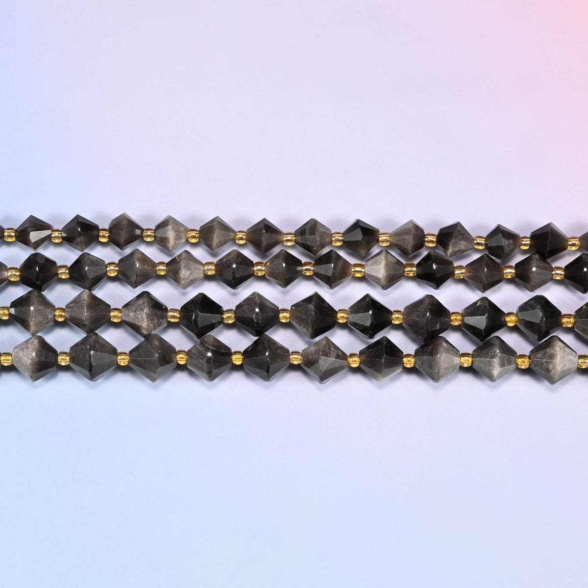 Silver obsidian bicone beads in straight rows, seen close up, each bead cut to two points meeting at a wide center.