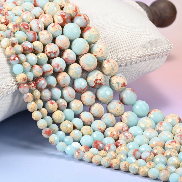 Dyed blue shoushan stone faceted round beads, light blue strands with tan and red-brown veining draped over a white cushion