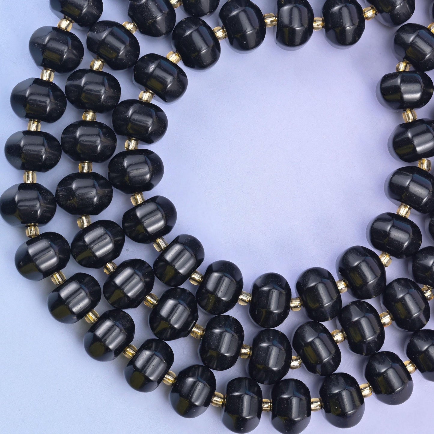 Overhead loop of obsidian pumpkin rondelles on a pale lavender surface