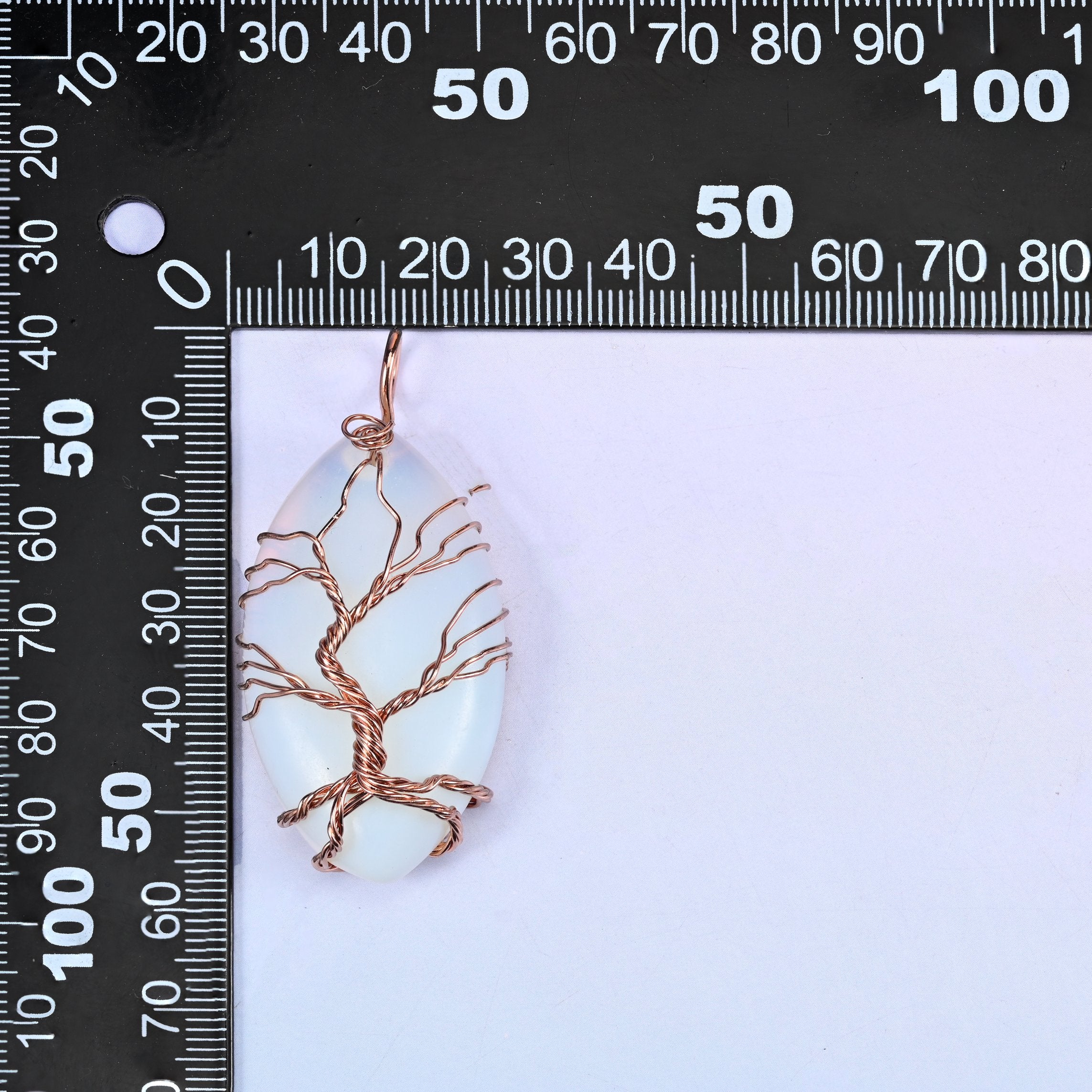 Oval Crystal Pendant with Copper Wired Tree placed against a black millimetre ruler for scale, the white piece measuring about 55x26mm.