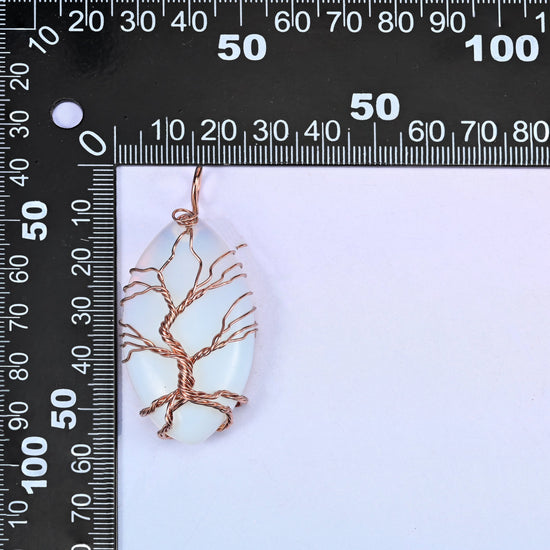Oval Crystal Pendant with Copper Wired Tree placed against a black millimetre ruler for scale, the white piece measuring about 55x26mm.