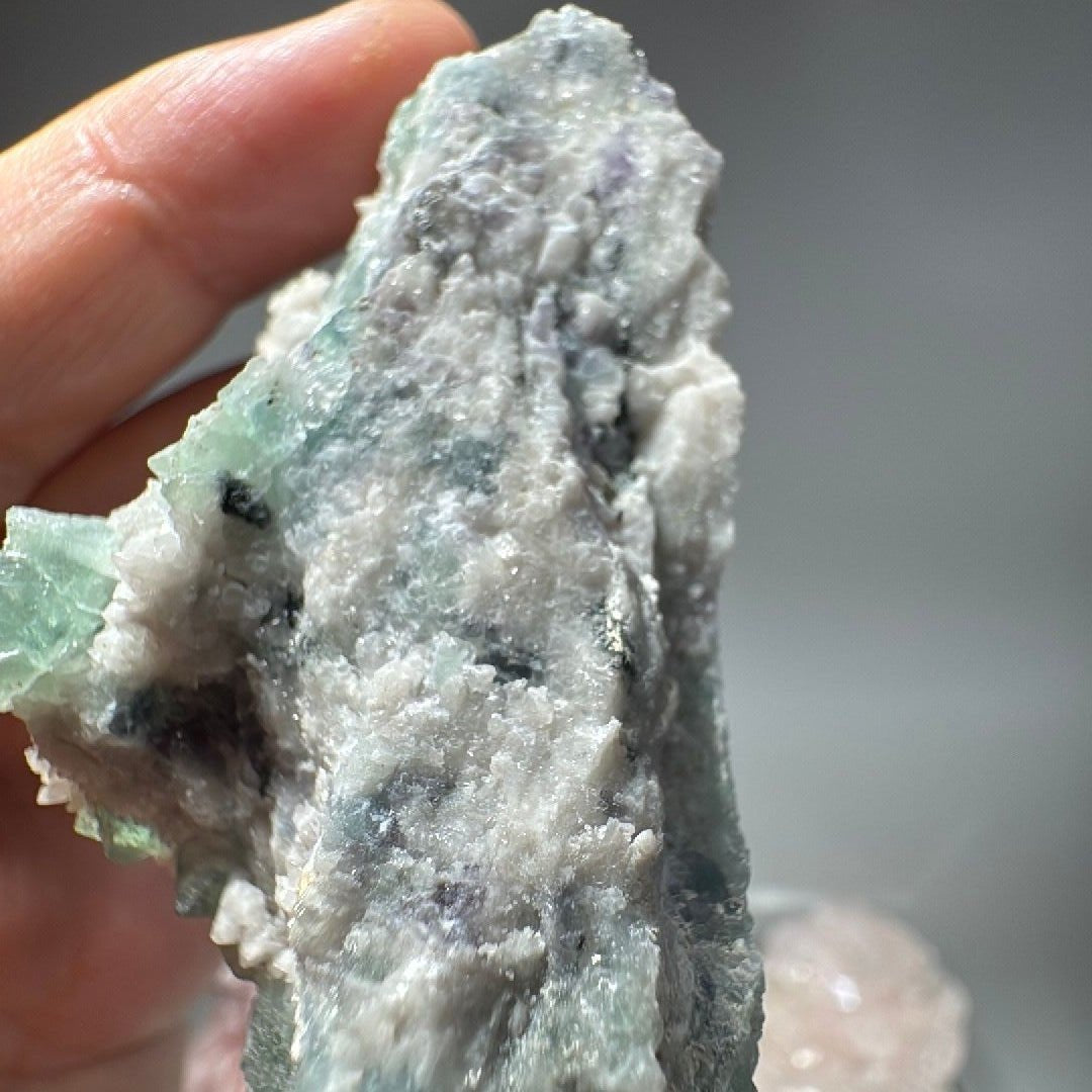 Reverse of the piece, mostly pale grey rock with a few green crystals along the rim