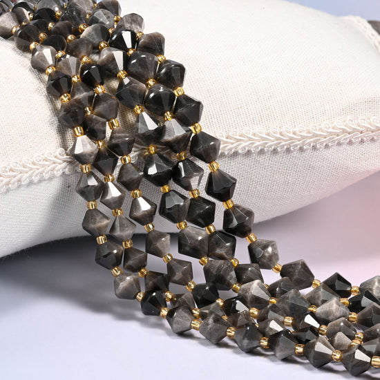Silver obsidian bicone beads laid out on the diagonal in several rows, smoky gray-black volcanic glass with a cool silvery sheen, a gold-tone spacer between every bead.
