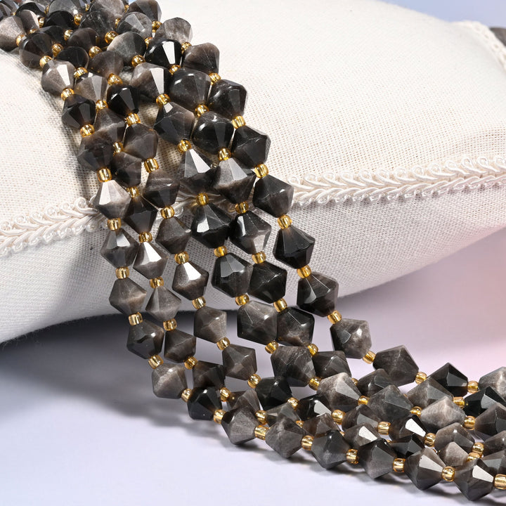 Silver obsidian bicone beads laid out on the diagonal in several rows, smoky gray-black volcanic glass with a cool silvery sheen, a gold-tone spacer between every bead.